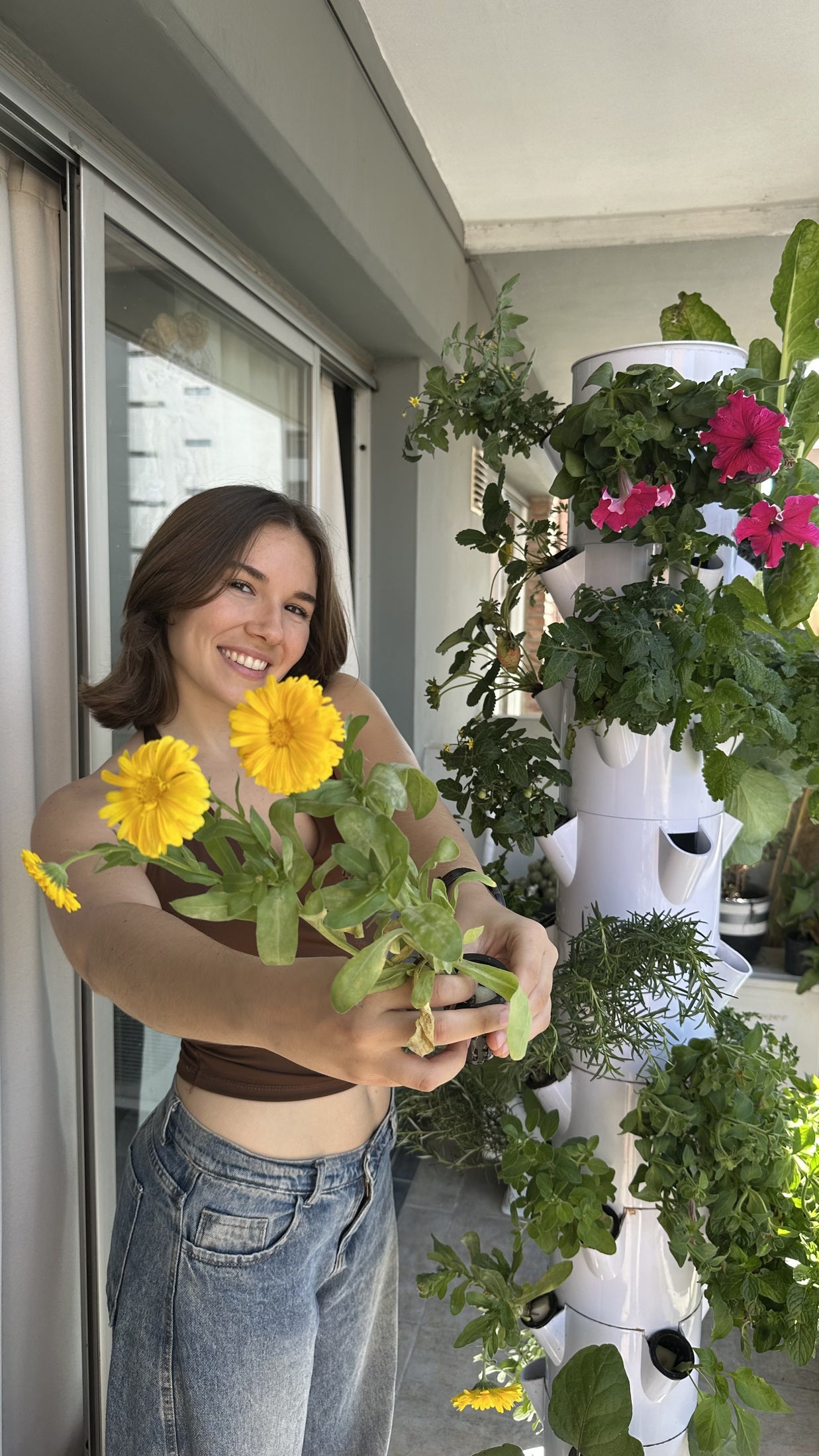 Mujer sosteniendo flores junto a una huerta vertical